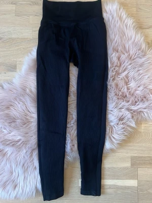 Svarta seamless tights från Stronger - Säljer ett par svarta leggings från Stronger i storlek XS/S. De har ribbad struktur och hög midja som sitter skönt och ger snygg siluett. Perfekta för träning eller chill. Materialet är mjukt och stretchigt syntet för maximal komfort.