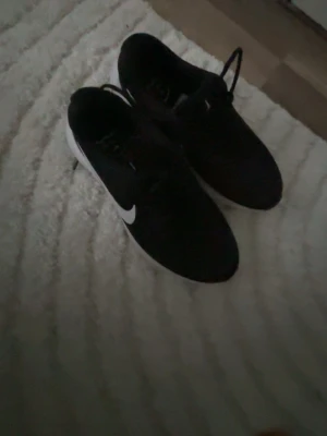 Svarta Nike träningsskor - Säljer ett par svarta Nike sneakers med vit sula och klassisk vit swoosh på sidan. Skorna har snörning och är tillverkade i syntetmaterial, perfekta för träning eller chill vardagsstil. Lätta och bekväma med sportig vibe.