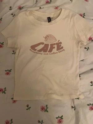 Vit t-shirt med café-tryck från H&M Divided - Säljer en vit t-shirt från H&M Divided i storlek XXS med coolt tryck på bröstet där det står 'CAFÉ Strawberry Hill Coffee Shop' och en jordgubbe. Aldrig använd