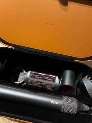 Dyson Airwrap multistyler och hårfön - Dyson multistyler och hårfön i metallicgrå och rosa med flera tillbehör, inklusive rundborste och olika munstycken. Kommer i en lyxig orange förvaringsbox med svart insida. Perfekt för att fixa håret med olika stylingalternativ personligt anpassat just för den hårstilen du föredrar. Skapar perfekta lockar och mycket volym. Multistyler är skonsamt använt och fungerar/ser ut som helt ny. 