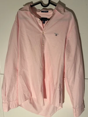Rosa Oxfordskjorta från GANT XL - Snygg rosa Oxfordskjorta från GANT. Skjortan har klassisk krage, knappar framtill och GANT-logga broderad på bröstet. Tillverkad i mjuk bomull som känns skön mot huden. Perfekt för dig som gillar stilrena och fräscha plagg.