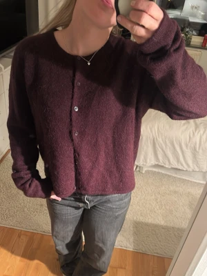 Mörklila stickad kofta med knappar - Säljer en mysig mörklila stickad kofta med rund hals och knappar framtill. Koftan har långärmade och en loose passform som gör den extra skön. Perfekt att slänga på sig när det är kyligt ute.