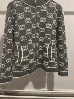 Grå stickad kofta från Gucci - Säljer en grå stickad kofta från Gucci med vitt GG-monogram över hela plagget. Koftan har ribbade muddar, två fickor framtill samt silverfärgad dragkedja med Gucci-logga. Storlek M men passar S – normal passform. Perfekt för dig som gillar lyxiga detaljer och clean design.  📌 Läs Plick-bio innan köp 📦 Ansvarar ej för PostNords/transportörens slarv efter att paketet är inlämnat ❌ Inga returer 💬 Seriösa affärer endast  Finns även ute på HypeTorget. 