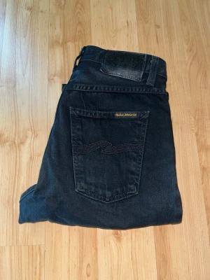 Nudie Jeans  - Snygga svarta baggy jeans från Nudie Jeans. Midja 32cm, längd 100cm. JAG SKICKAR EJ FLER BILDER NÄR JAG BÄR JEANSEN! för bättre inblick i passformen rekommenderar jag att googla på modellnamnet. För storleksguide kolla måtten noggrant då jeansen alltid kan vara uppsydda heller krympta och jag ej tar emot returer :) s5,4