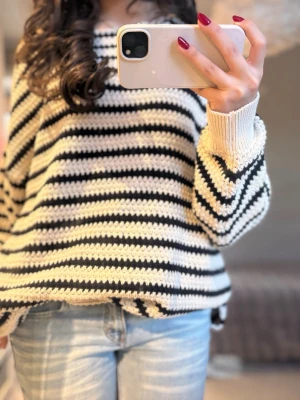 Randig stickad tröja i oversized modell - Säljer en riktigt skön stickad tröja med svarta och vita ränder. Tröjan har en loose och oversized passform, rund hals och långa ärmar med ribbade muddar. Perfekt att slänga på sig när det är lite kyligt ute.