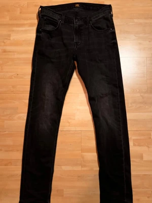 Lee jeans - Svarta jeans från Lee i modellen Luke, slim fit passform. Klassisk femficksdesign med Lee-logga på bakfickan. Jeansen är gjorda i ett mjukt bomullsmaterial med lite stretch för extra komfort. Perfekt för dig som gillar stilrena och tidlösa jeans.