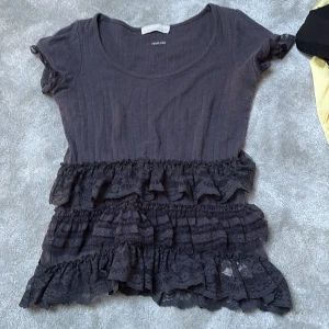 Svart blus med spetsvolanger - Säljer en svart blus från odd Molly med korta ärmar och rund halsringning. Toppen har ribbad struktur och flera lager med spetsvolanger nedtill och vid ärmsluten, vilket ger en cool och romantisk vibe. Perfekt för dig som gillar detaljer och vill sticka ut.