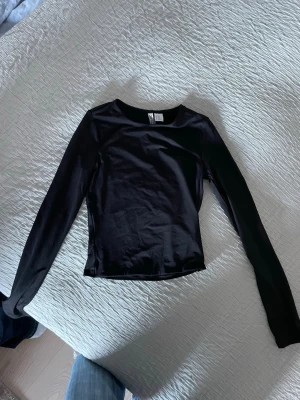 Svart långärmad topp från H&M Divided - En stilren svart långärmad topp från H&M Divided i storlek XXS. Toppen har en rund halsringning och är figurnära i modellen. Materialet är mjukt och stretchigt, perfekt för att matcha med jeans eller kjol. Enkel och snygg basic som funkar till många olika looks. Helt ny!