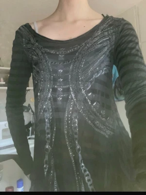 Svart långärmad topp Miss Me M - Svart långärmad topp från Miss Me i storlek M. Toppen har glittriga detaljer och ett randigt mönster, samt en öppen rygg och en U-formad skärning vid halsen. Materialet är mjukt och lätt, med silvriga detaljer och studds.