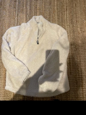 Beige teddyjacka från Kappahl - Mysig beige teddyjacka från Kappahl med halv dragkedja och hög krage. Jackan är fluffig och har en relaxed vibe, perfekt för kyliga dagar. Detalj med svart zip puller där det står 'UNIQUE'.