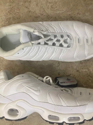 Nike Air Max Plus vita sneakers - Nike Air Max Plus sneakers i helvit färg med TN-logga på hälen och sulan. Skorna har en mesh- och syntetöverdel, synliga Air Max-bubblor i sulan och snörning framtill. Snygg vågig design på ovansidan och robust svart yttersula. Endast hos Foot Locker.