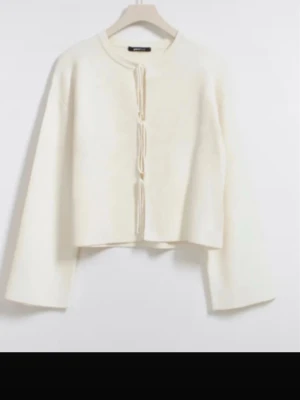 Vit kofta med snörning från Gina Tricot - Säljer en vit kofta från Gina Tricot med snygg snörning framtill. Koftan har långärmade, vida ärmar och är croppad i modellen. Perfekt att styla med jeans eller kjol för en trendig look. Storek xs