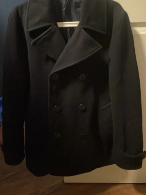 Mörkblå skepparkavaj från M&S, stl S - Klassisk mörkblå skepparkavaj från M&S med dubbelknäppning och breda slag. Jackan har en stilren look med knappar framtill och diskreta fickor på sidorna. Perfekt för dig som gillar tidlös och snygg stil under kyliga dagar. Vid eventuella frågor är det bara att höra av sig!