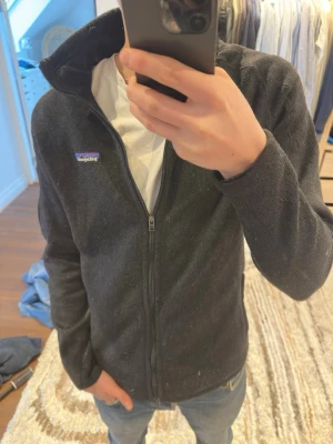 Svart fleece från Patagonia - Svart fleece från Patagonia i storlek S med hel dragkedja framtill och en extra dragkedja på ärmen. Klassisk logga på bröstet och insidan är mjuk fleece. Perfekt för kyliga dagar!! Köptes 2022 för runt 1500 men har bara använts enstaka gånger. Bara att skriva om det finns några frågor eller om fler bilder behövs🤗