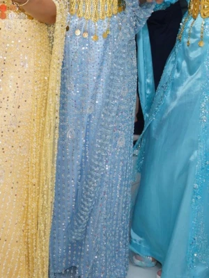 Blå kurdisk klänning - Säljer en ljusblå långklänning med glittrigt paljettmönster och detaljerade broderier. Klänningen har långärmade transparenta ärmar.