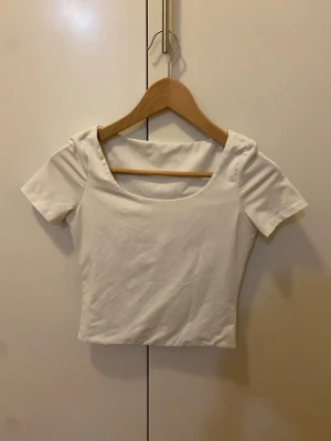 Vit T-shirt - Säljer en enkel och stilren vit croppad topp med korta ärmar och bred rund ringning. Toppen är figurnära och gjord i mjukt bomullsmaterial som sitter skönt mot kroppen. Strl S