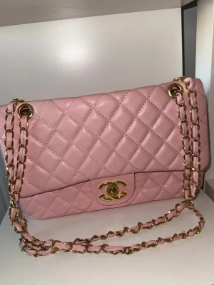 Rosa söt liten märkes axelväska - Säljer en ikonisk rosa axelväska i skinn med quiltad design och guldfärgad kedja. Väskan har klassisk CC-låsning framtill och snygga detaljer som ger en lyxig vibe. Perfekt storlek för det viktigaste och en riktig statement piece för din outfit. Aldrig använd. 