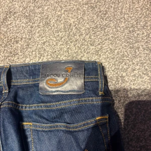 Jacob Cohen blå jeans Style 688 - Snygga blå jeans från Jacob Cohen, Style 688. Klassisk femficksmodell med gul kontrastsöm och broderad J på myntfickan. Jeansen har knappgylf och exklusiva detaljer på insidan. Perfekt för dig som gillar stilrena och kvalitativa jeans. Använda några gånger är i nyskick