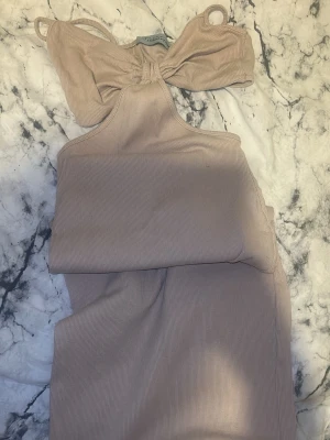 Beige ribbad långklänning med rosett - Säljer en beige ribbad långklänning från Industry med snygg rosettdetalj framtill och smala axelband. Klänningen har en omlottliknande överdel och är tillverkad i mjukt, stretchigt material som sitter bekvämt. Perfekt för dig som gillar stilrena och trendiga plagg. Öppen rygg, kan visa bättre bilder. 