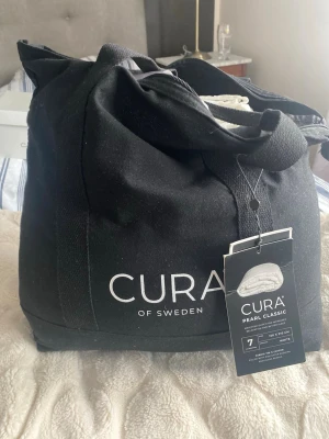 Vit quiltad tyngdtäcke från Cura of Sweden - Säljer en vitt Tyngdtäcke från Cura of Sweden. Täcket är tillverkad i 100% bomull med polyesterstoppning och glaspärlor, vilket ger en tyngd och skön känsla. Den har en stilren design med diskret logga och passar perfekt för dig som gillar minimalistisk stil.