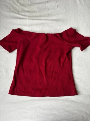Mörkröd offshoulder topp - Säljer en mörkröd offshoulder topp i mjuk bomull. Toppen har korta ärmar och en figurnära passform som ger en snygg siluett. Perfekt att styla med jeans eller kjol för en trendig look.