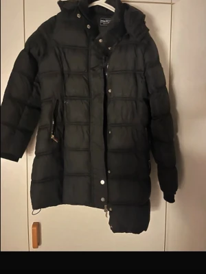 Black padded winter jacket  -  Stylish black padded jacket in good condition. But it have been used. Classic quilted design with a sleek metal triangle logo on the sleeve. Perfect for autumn and winter – warm, comfortable and easy to style. Ideal for everyday wear or a more dressed-up look. Selling because it’s no longer used. The jacket says size 160 but it fits me and i have S/M Price can discuess   