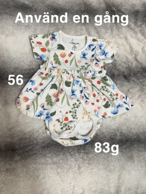 Vit blommig babyklänning med inbyggd body Polarn O. Pyret - Supersöt vit babyklänning med inbyggd body från Polarn O. Pyret med färgglatt blommigt mönster i blått, rosa, grönt och rött. Kortärmad modell med inbyggd body och tryckknappar vid axeln. Perfekt för små äventyrare som gillar färg och mönster.🌸Använd en gång. Storlek 56. 