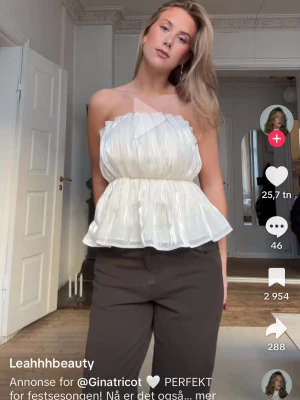 Vit bandeau tubtopp med volang - Superfin vit bandeau tubtopp med volangkant och lätt glansigt tyg. Toppen är ärmlös och har en luftig, flowy passform med markerad midja. Perfekt för sommarens alla tillfällen och enkel att styla med jeans eller kjol.