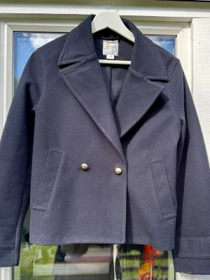 Marinblå kortare kappa från Gina Tricot  - Säljer en marinblå kortare kappa från Gina Tricot. Jättesnygg jacka att ha nu på våren och senare till hösten.