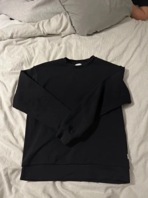 Svart sweatshirt från Jack & Jones - Svart sweatshirt från Jack & Jones med klassisk rund hals och långa ärmar. Tröjan har ribbade muddar vid ärmslut och nederkant, och är gjord i mjuk bomull. Perfekt för chill dagar och enkel att matcha med jeans eller joggers.