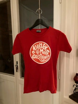 Röd vintage t-shirt med tryck - Röd vintage t-shirt från Clique i storlek L med ett stort retroinspirerat tryck på bröstet där det står 'Kärlek, Makt, Systerskap' i vitt säljes för 150kr. Trycket med med tiden spruckit något vilket syns på sista bilden, annars är tröjan i gott skick. Det står storlek L men jag uppskattar storleken till S/M. 