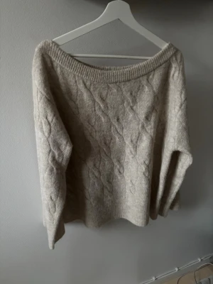 Beige stickad tröja Gina Tricot - Mysig beige stickad tröja från Gina Tricot i storlek M. Tröjan har ett klassiskt flätmönster, rund halsringning och långa ärmar. Perfekt för kyliga dagar och enkel att matcha med olika outfits.