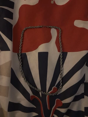 Silvrig kedja 48 cm - Säljer en silvrig kedja med tvinnad design, perfekt längd på 48 cm. Kedjan har ett smidigt lås och passar dig som gillar stilrena accessoarer med lite edge. Materialet är fullt 925/92,5% silver och den andra 75/7,5 är Palladium. Köpte den för  1200kr säljer den för 600kr