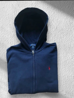 Blå Ralph Lauren Zip Hoodie - Klassisk Ralph Lauren hoodie i blå färg. Tröjan är i mycket bra skick. Sparsamt använd :-) |  Bröstvidd, (pit to pit): 52 cm | Längd: 64 cm |  Storlek: S (XL i barnstorlek men lika stor som S) | Skick: Mycket bra skick! | Färg: Blå | Märke: Ralph Lauren | Modell: Hoodie |  Hör gärna av dig vid frågor så svarar jag så fort jag kan! 😁|  