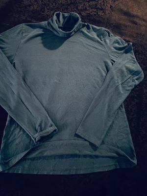 Mörkgrön polotröja i bomull - Säljer en enkel och stilren mörkgrön polotröja med lång ärm och hög krage. Tröjan är tillverkad i mjuk bomull och har en rak passform som är skön att bära. Perfekt att matcha med jeans eller under en jacka.