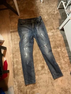 Jeans med slitningar - Snygga jeans med slitningar i färgen blå. Är 29/34 i längd men jag har haft dem som 30/32. Hör av er vid frågor😊
