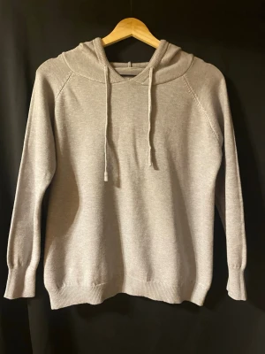 Mjuk ljusgrå stickad hoodie - Ljusgrå stickad hoodie i mjukt och behagligt material. Klassisk modell med huva och dragsnören, ribbade muddar vid ärmslut och nederkant. Tunnare stickning – perfekt för vår/höst eller som lager. I fint skick utan synliga fläckar eller skador. Enkel att matcha till både jeans och mjukisbyxor för en avslappnad look.