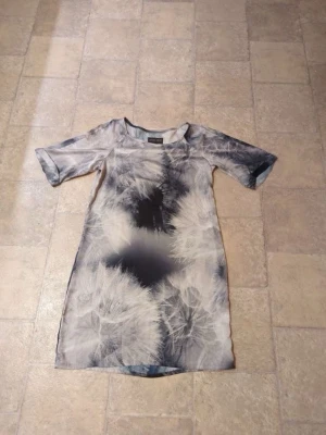 Kort klänning från Wivica Oest - Unik kort klänning från Wivica Oest med abstrakt mönster i svart, grått och vitt. Klänningen har rund halsringning och korta ärmar. Materialet känns lätt och svalt, perfekt för dig som gillar en modern och konstnärlig stil.