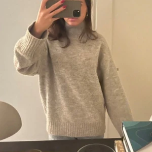 Beige stickad polotröja - Mysig beige stickad polotröja med breda ribbade muddar och hög krage. Tröjan har en loose passform och är perfekt för kyliga dagar. Enkel att matcha med jeans eller kjol för en avslappnad stil.