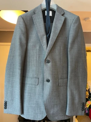 Grå 3 delad kostym, storlek 46 - Säljer en stilren grå kostym från Bläck i storlek 46. Kostymen består av kavaj, väst och byxor i ett diskret vävt mönster. Skräddarsydd passform med klassiska detaljer som knappar framtill och fickor med lock. Perfekt för dig som vill ha en clean och modern look. Använd ett fåtal gånger