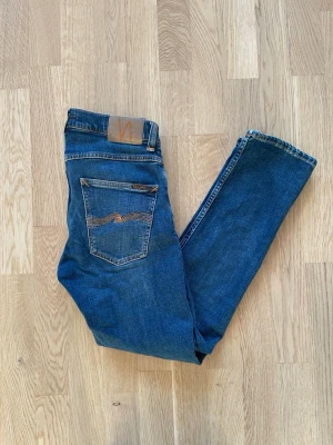 Blå Nudie jeans Grim Tim W30 L30 - Jag säljer dom här riktigt snygga Nudie Grim Tim jeansen som är i storlek W30 L30. Dessa är i riktigt fint skick men de har en defekt som syns på sista bilden. Men den defekten är inte så stor och man tänker inte på den alls. Tveka inte att höra av er!                                                                     Mått: Längd=100cm. Midja=40cm