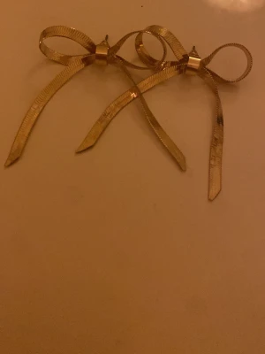 Guldrosett örhängen - Säljer ett par snygga örhängen i form av rosetter i guldtonad metall. De har en tunn och glansig finish som ger en cool och trendig vibe. Perfekta för att lyfta din outfit med en unik detalj. Rosetterna är lätta och sitter bekvämt på örat. Oanvända 😊