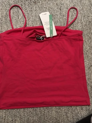 Rosa linnetopp från Gina Tricot - Säljer en snygg rosa linnetopp från Gina Tricot i modellen Scarlet Singlet. Toppen har tunna axelband och är rak i modellen, perfekt till sommaren eller en tjejkväll . Färgen är stark och sticker verkligen ut. Materialet är mjukt och skönt, troligtvis bomull eller en bomullsblandning. Helt ny !!