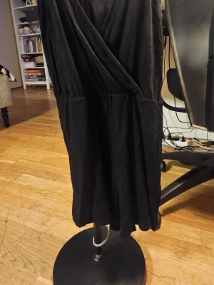 Svart byxkjol från NLY Trend - Svart kort byxkjol från NLY Trend med omlott-design och djup v-ringning.  har en mjuk och lätt polyesterkvalitet som faller snyggt. Perfekt för dig som gillar stilrena och enkla plagg med en modern touch.