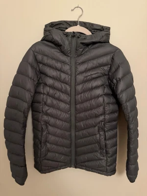 Olivgrön dunjacka Peak Performance - Dunjacka från Peak Performance i storlek S. Jackan har huva, dragkedja framtill och två sidofickor. I väldigt bra skick! ORDINARIE PRIS: 2000kr