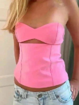 Rosa korsett-topp med cut out - Säljer en snygg rosa korsett-topp med axelbandslös design och cool cut out-detalj under bysten. Toppen är figurnära och croppad, perfekt till jeans eller kjol. Materialet känns slätt och stretchigt, vilket gör den bekväm att bära.
