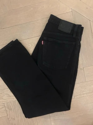 Levi's  Straight svarta jeans - Svarta Levi's Premium Wedgie Straight jeans i klassisk femficksmodell med raka ben och hög midja. Sitter väldigt snyggt på. Jeansen har knappgylf med silverfärgade och kopparfärgade detaljer samt Levi's röda etikett på bakfickan. Materialet är slitstarkt jeans i bomull.