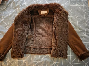 Brun teddyjacka från Vila, storlek M - Säljer en brun teddyjacka från Vila med mjukt fuskpälsfoder och detaljer i mockaimitation. Jackan har dragkedja, dekorativa knappar och två snedställda fickor med dragkedja. Snygg krage och muddar i samma fluffiga material för extra mysfaktor.