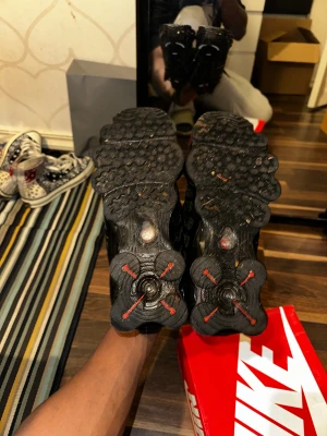 Nike Shox svarta sneakers - Nike Shox sneakers i helsvart med röda detaljer på tungan och sulan. Skorna har en unik fjädrande Shox-sula, mesh- och syntetpaneler samt snörning. Snyggt sportig design med rund tå och platt sula, perfekt för dig som gillar att sticka ut med dina kicks.