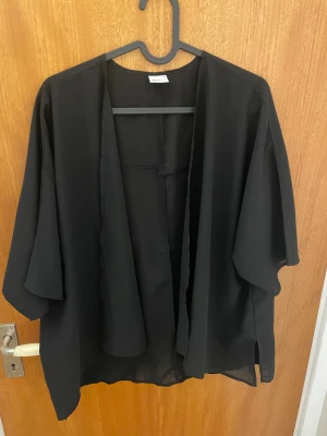 Kofta Gina tricot  - Säljer en svart, luftig lite genomskinlig kofta från Gina Tricot i storlek S. Perfekt att ha över en topp för en chill och stilren look.